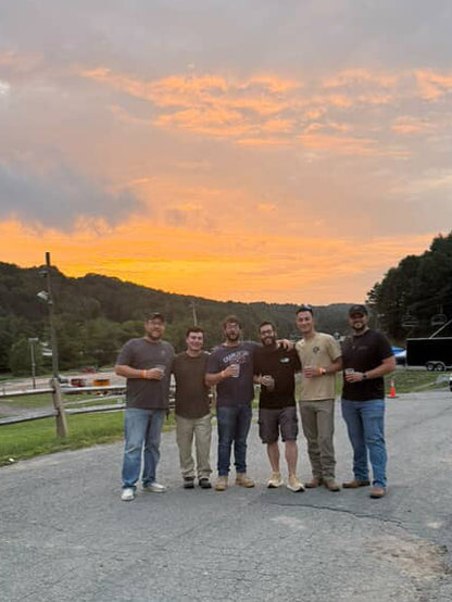 Group of six men standing on a road at sunset with a colorful sky.
